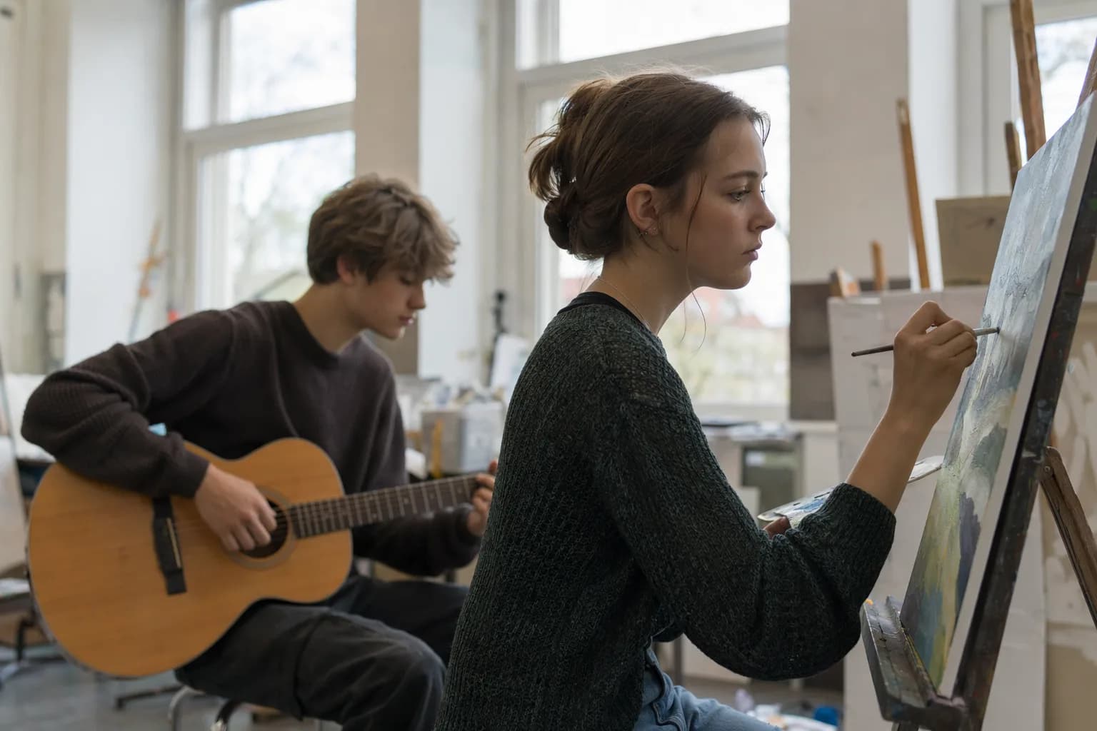 Zwei Oberstufenschüler in einem Kunstraum, einer malt an einer Staffelei, während die andere im Hintergrund Gitarre spielt (mit KI erzeugtes Bild)