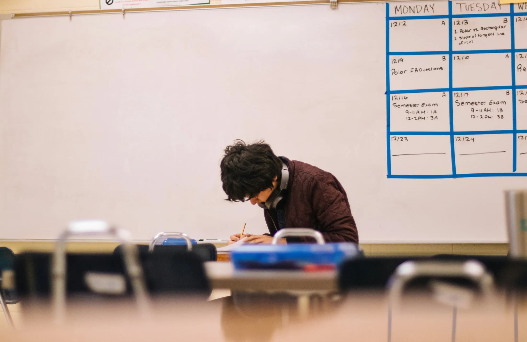 Schüler arbeitet konzentriert an einem Tisch vor einer Tafel mit Prüfungsplan