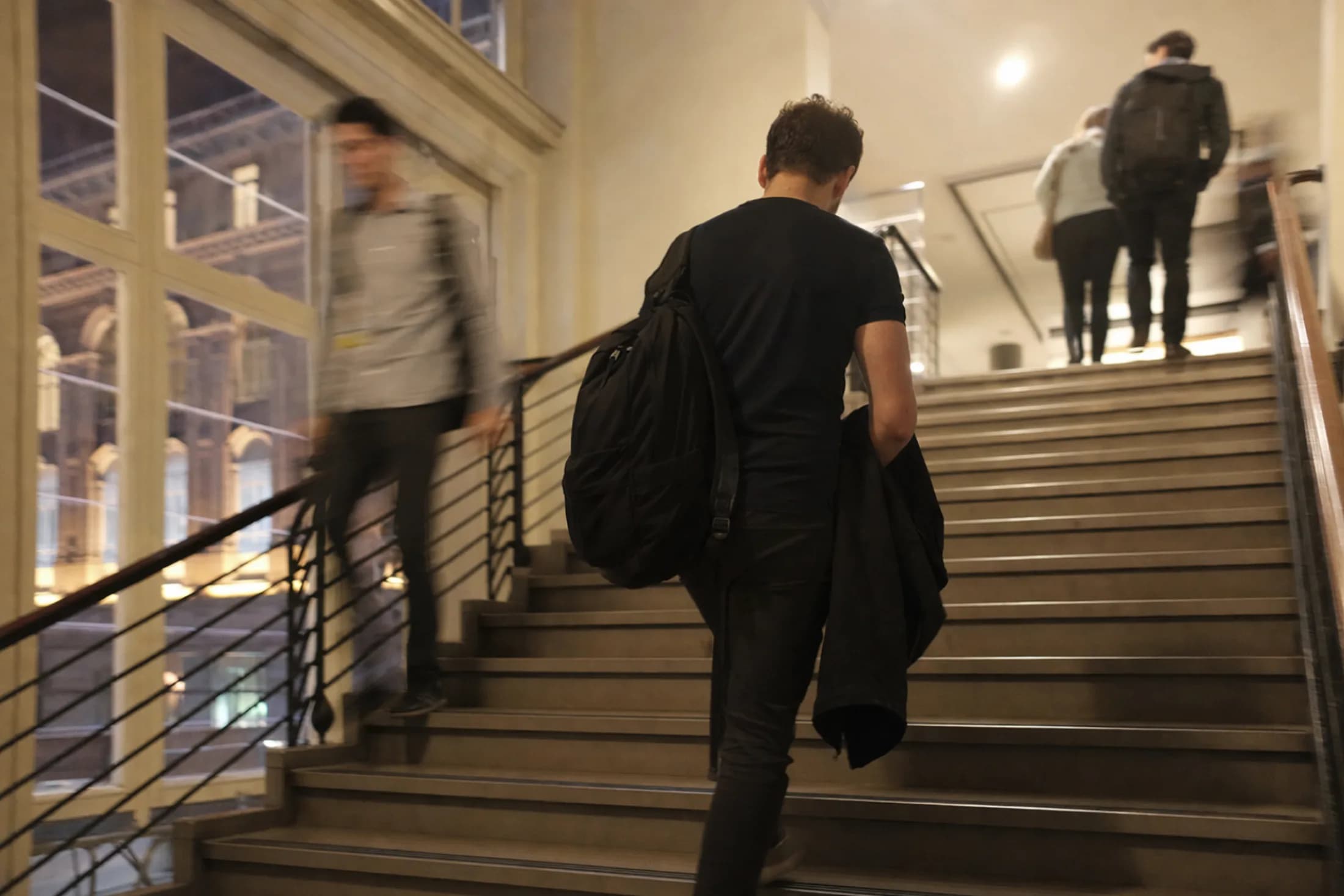 Erwachsener steigt am Abend mit Rucksack und Jacke die Treppe eines Schulgebäudes hinauf (mit KI erzeugtes Bild)