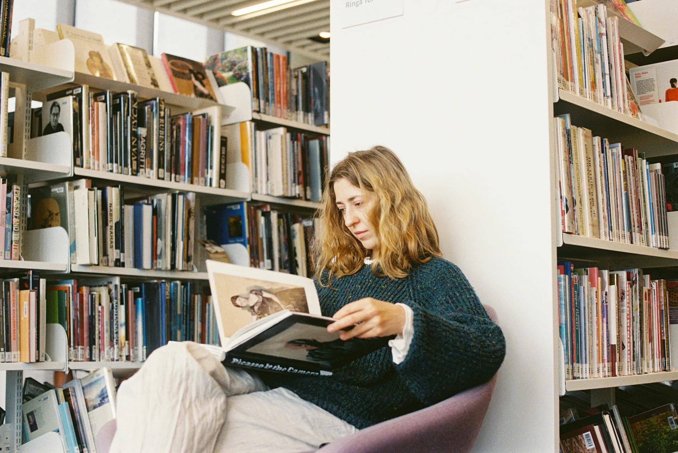 Junge Frau liest ein Buch zwischen hohen Bücherregalen