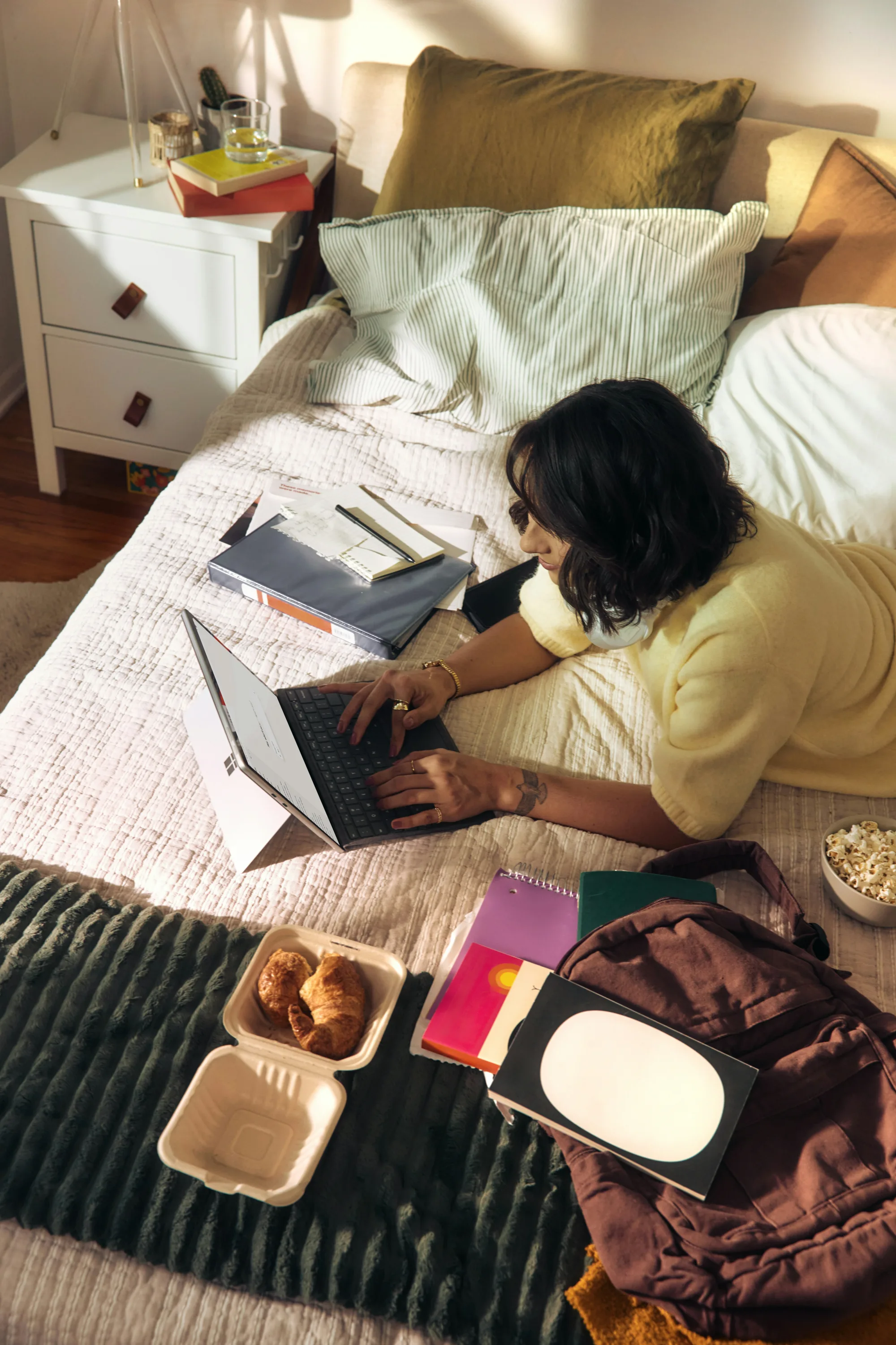 Schülerin lernt mit Laptop und Unterlagen im Bett für das Abitur