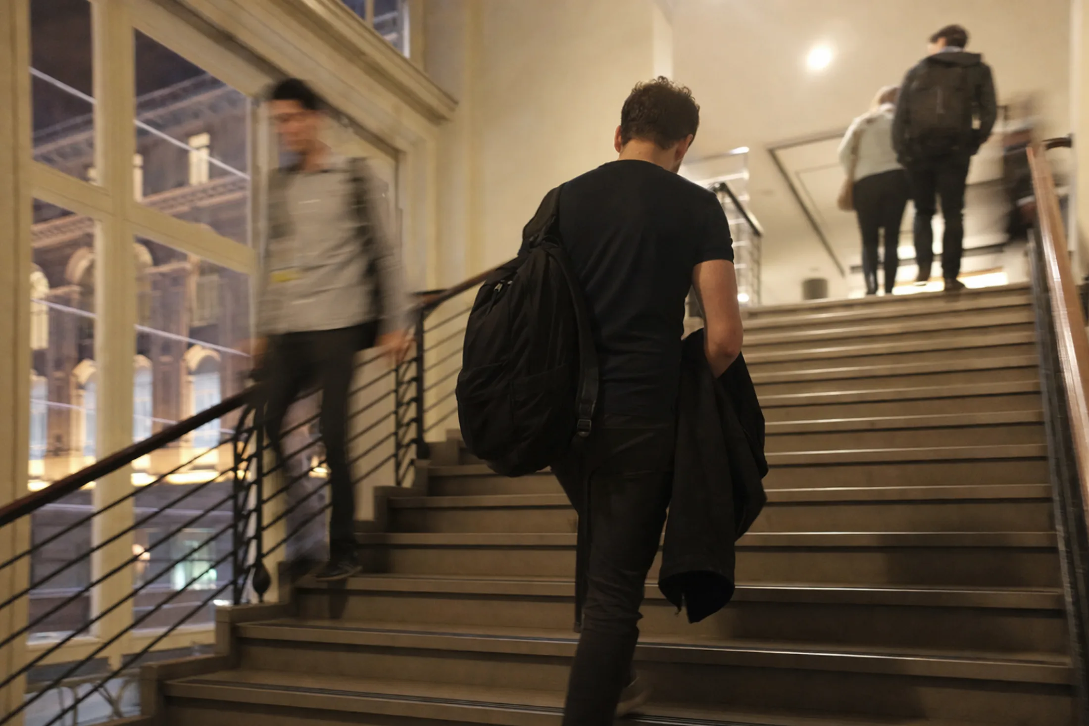 Erwachsener steigt am Abend mit Rucksack und Jacke die Treppe eines Schulgebäudes hinauf (mit KI erzeugtes Bild)