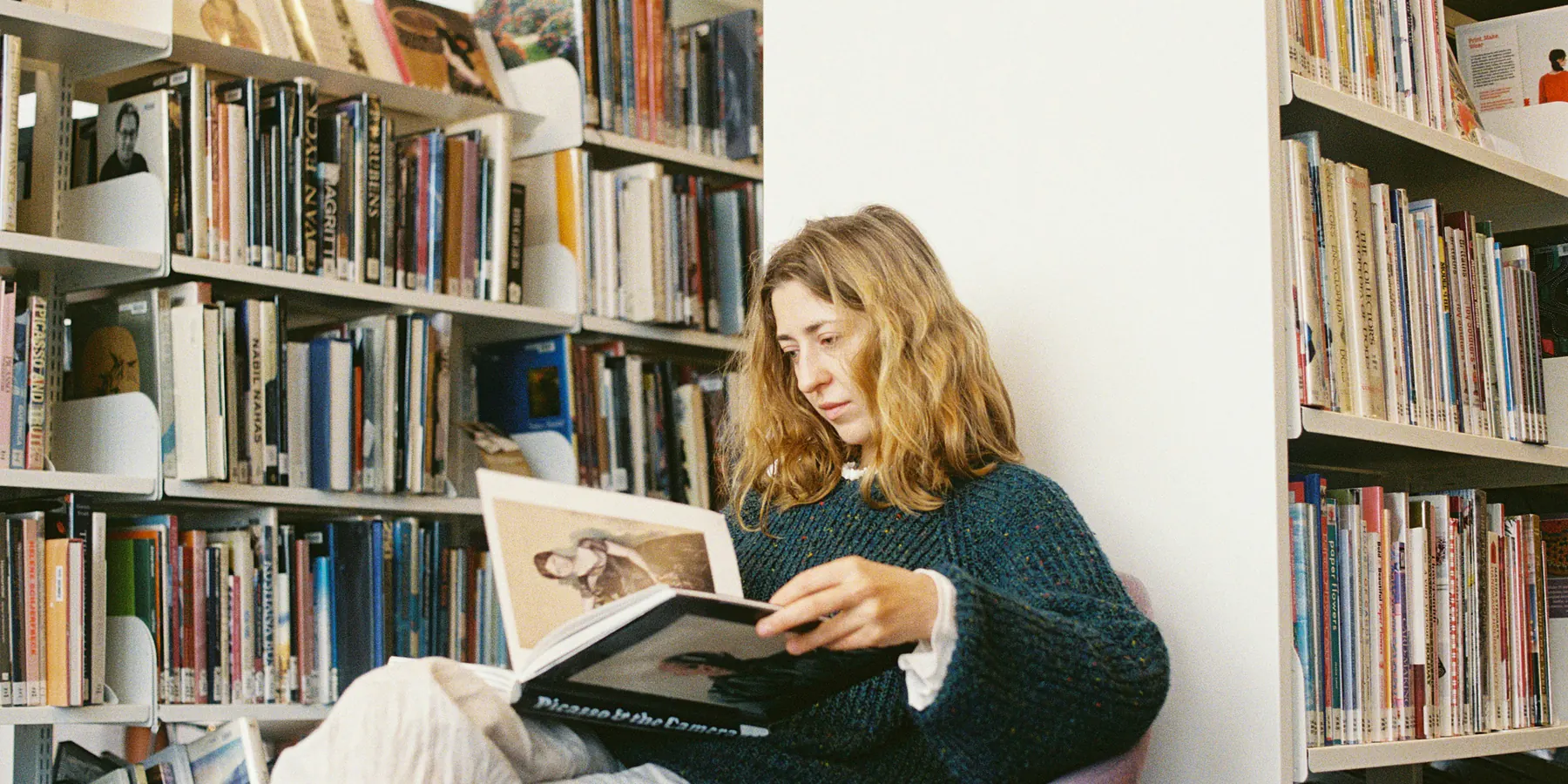 Eine Frau liest ein Buch zwischen gefüllten Bücherregalen in einer Bibliothek
