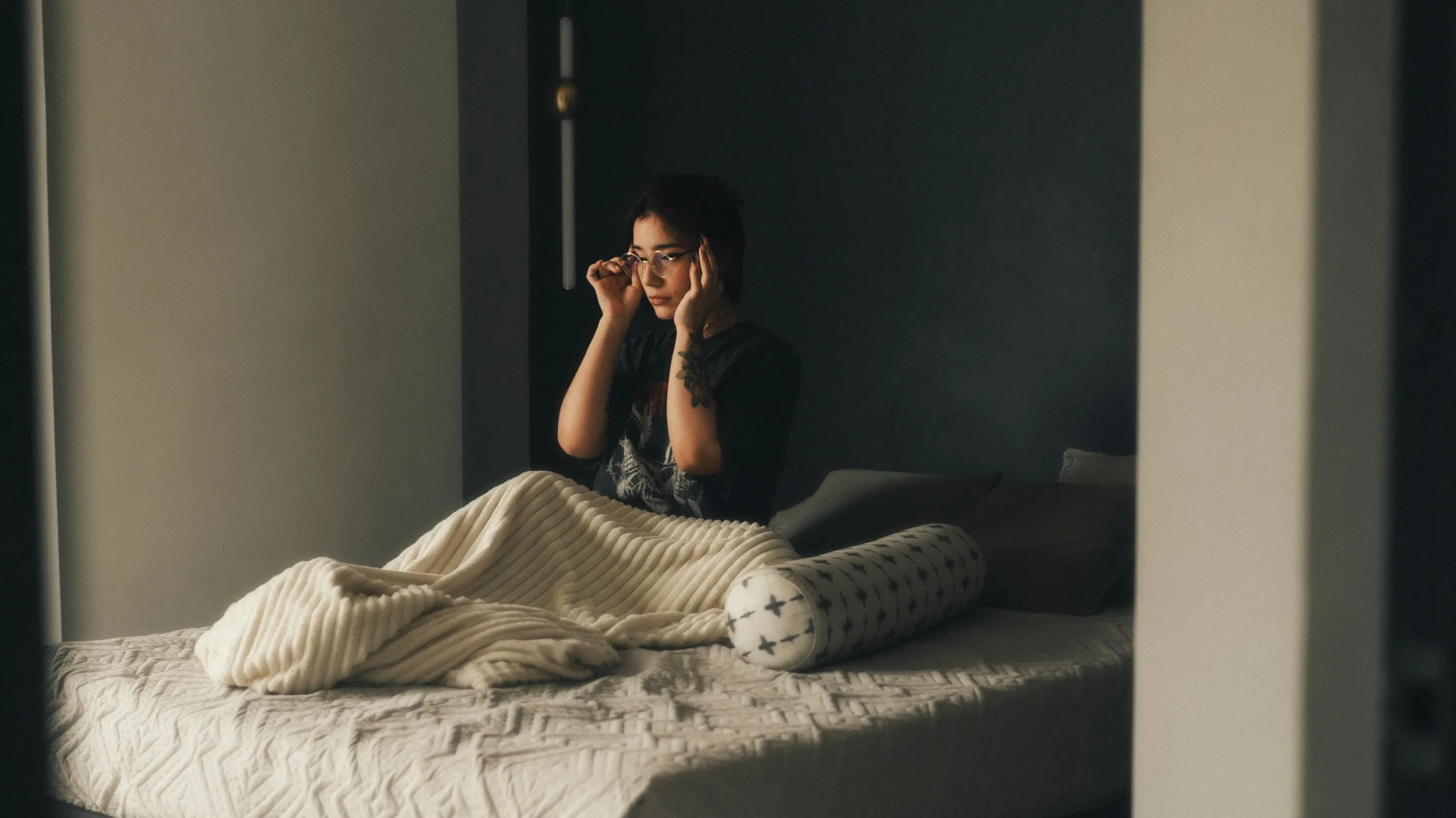 Junge Person sitzt nachdenklich auf einem Bett in gedämpftem Licht